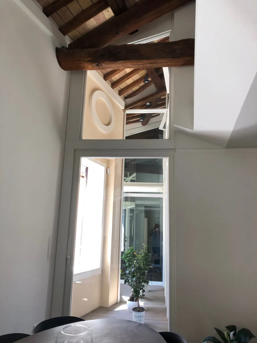 Interno con travi lignee, pareti vetrate e passaggio verso un patio