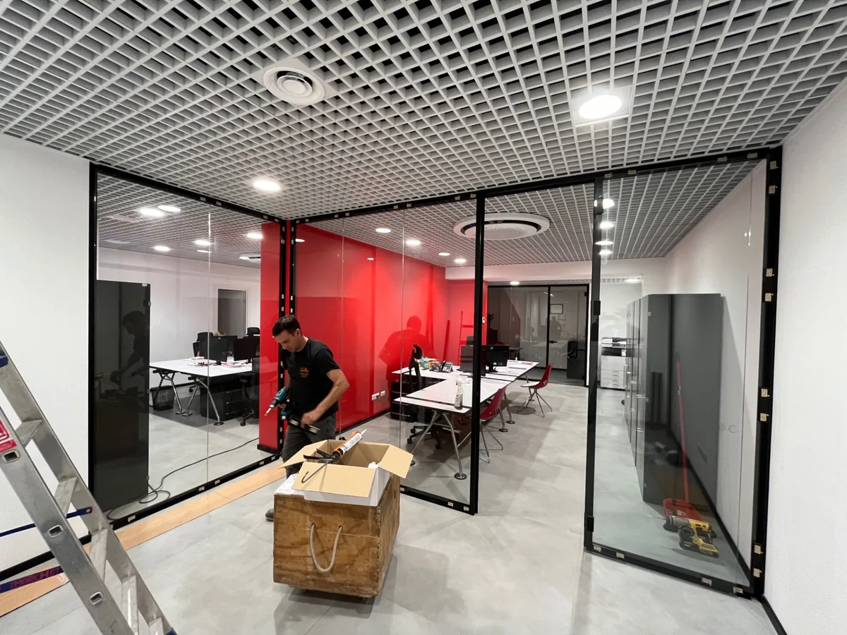 Uffici completati con partizioni vetrate, parete rossa e controsoffitto a griglia