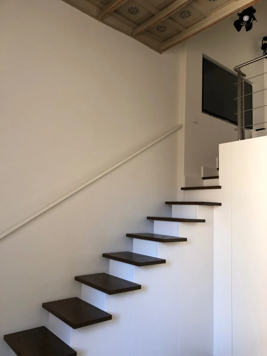 Scala con pedate lignee scure e parapetto bianco sotto soffitto decorato