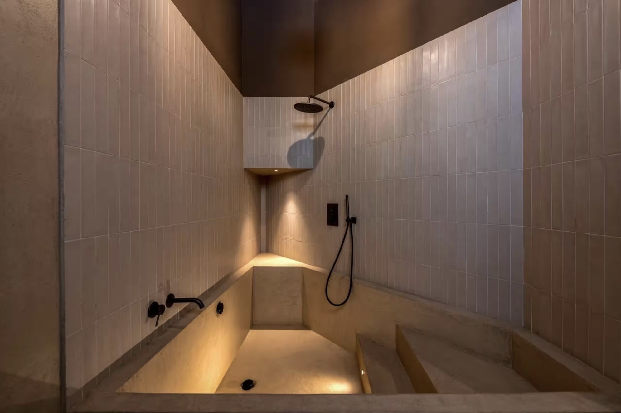 Ambiente bagno con vasca in muratura, doccia e rivestimento chiaro