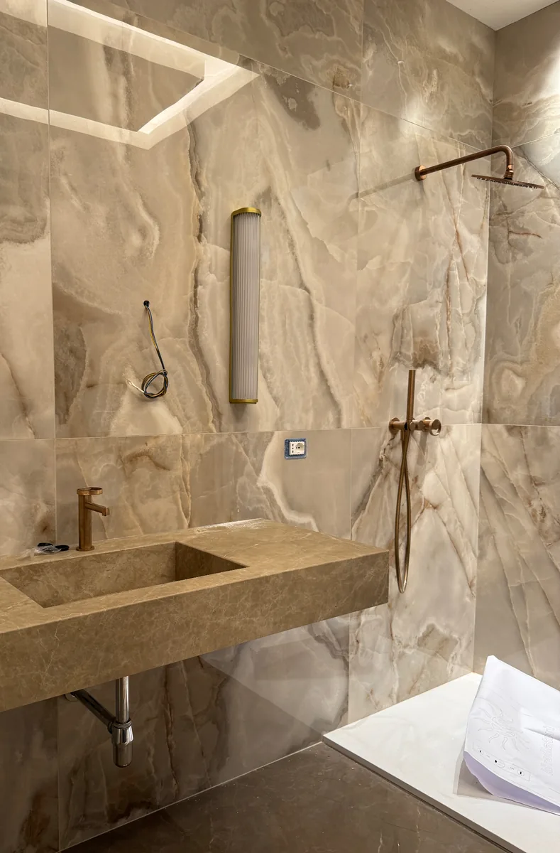 Bagno con lavabo integrato in pietra, grandi lastre venate e rubinetteria in rame